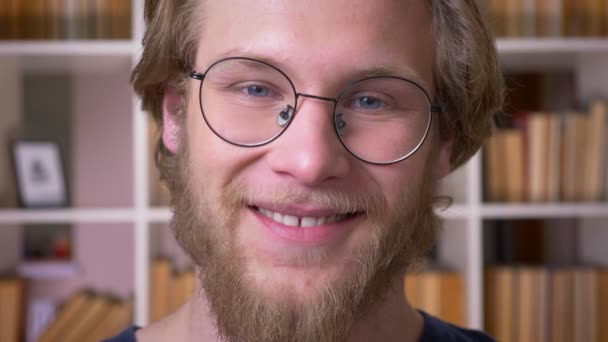 Close-up shoot van volwassen aantrekkelijke Kaukasische mannelijke student in glazen glimlachend op zoek naar camera in de Universiteitsbibliotheek binnenshuis — Stockvideo