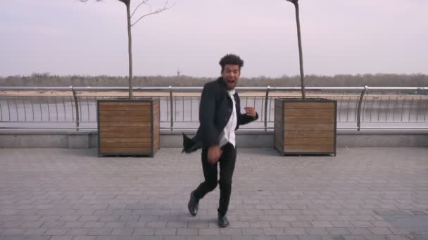 Primer plano vista recta retrato de joven atractivo afroamericano hombre bailando y haciendo movimientos de barajar mirando a la cámara en la calle en la ciudad urbana — Vídeo de stock