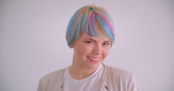 Fille caucasienne extraordinaire aux cheveux multicolores et aux sourires perçants timidement dans la caméra sur fond blanc . — Video