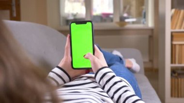 Yeşil ekran ile telefonda kadın mesajlaşma Closeup geri görünüm çekimi dikey rahat bir dairede kapalı kanepeüzerinde döşeme tutarak