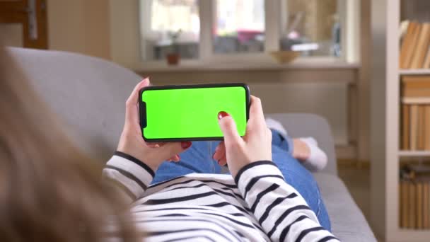 Närbild tillbaka Visa shoot av kvinnlig rullning telefonen med grön skärm håller den horisontellt om på soffan inomhus i en mysig lägenhet — Stockvideo