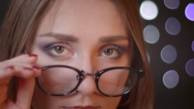 Genç güzel beyaz kız kamera bakarak ve bokeh arka plan ile gülümseyen gözlük sabitleme Closeup portre