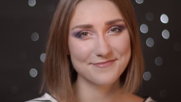 Retrato de close-up de jovem menina bonita caucasiana olhando para a câmera e sorrindo com fundo bokeh — Vídeo de Stock