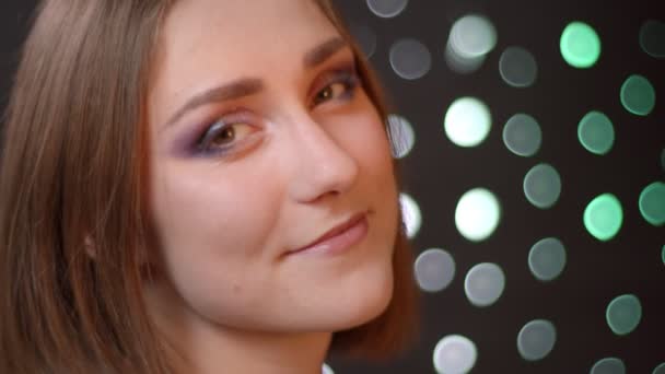 Nahaufnahme Porträt des jungen netten kaukasischen Mädchens, das in die Kamera schaut und freudig mit Bokeh-Hintergrund lächelt — Stockvideo