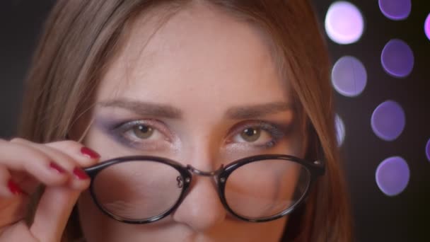 Close-up portret van jonge mooie Kaukasische meisje vaststelling van haar bril en het verhogen van wenkbrauw kijken naar camera flirten gelukkig met bokeh achtergrond — Stockvideo