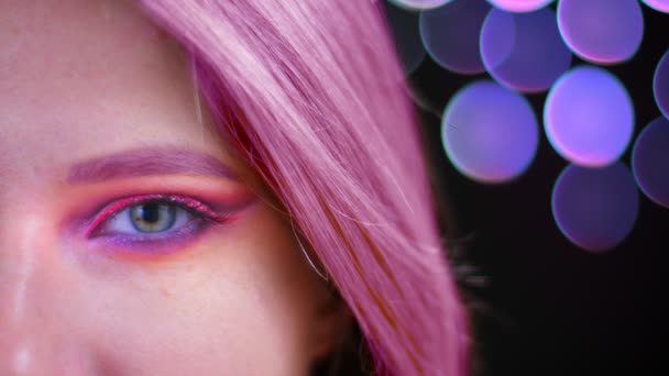 Closeup metade tiro rosto de jovem atraente mulher caucasiana com rosa bela maquiagem brilho rosa com cabelo rosa olhando para a câmera com fundo bokeh — Vídeo de Stock