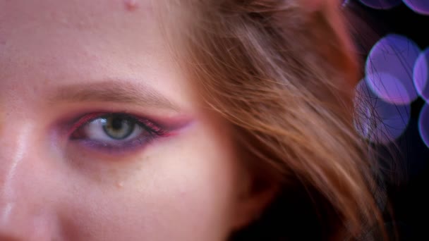 Nahaufnahme Shooting der jungen attraktiven kaukasischen weiblichen Gesicht mit halb aufgetragen glitzernden rosa Make-up Blick in die Kamera mit Bokeh-Lichter auf dem Hintergrund — Stockvideo