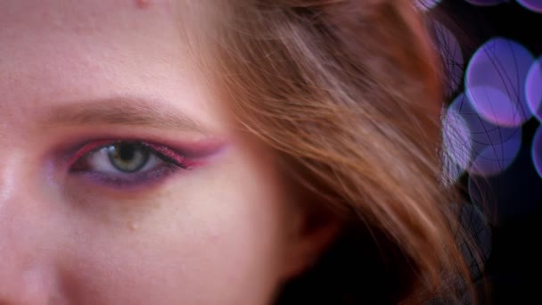 Primer plano de brote de joven hermosa cara femenina caucásica con medio aplicado brillo maquillaje rosa mirando a la cámara con luces bokeh en el fondo — Vídeo de stock