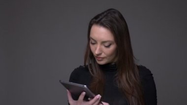 Güzel esmer kadın gri arka planda izole uygulama tavsiye etmek için kameraya tablet yeşil renk ekran gösterir.
