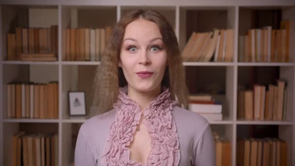 Retrato de una guapa profesora rubia de pelo ondulado con ojos ondulados siendo extremadamente divertida y sorprendida en la biblioteca . — Vídeo de stock