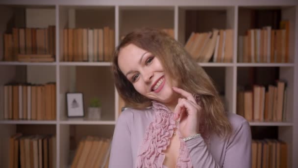 Portrait d'enseignant blond aux cheveux ondulés caucasiens posant joyeusement et séduisamment devant la caméra à la bibliothèque . — Video