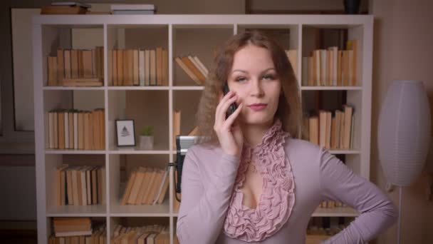 Πορτρέτο του Καυκάσου ξανθιά δασκάλα μιλάει στο κινητό τηλέφωνο προσεκτικά στη βιβλιοθήκη. — Αρχείο Βίντεο