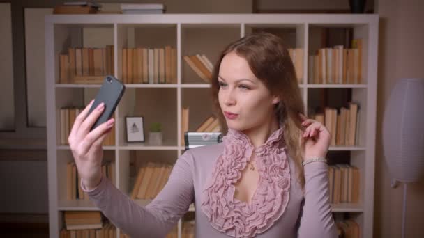 Πορτρέτο του Καυκάσου ξανθιά δασκάλα κάνει σαγηνευτικό selfie φωτογραφίες σε κάμερα στη βιβλιοθήκη. — Αρχείο Βίντεο