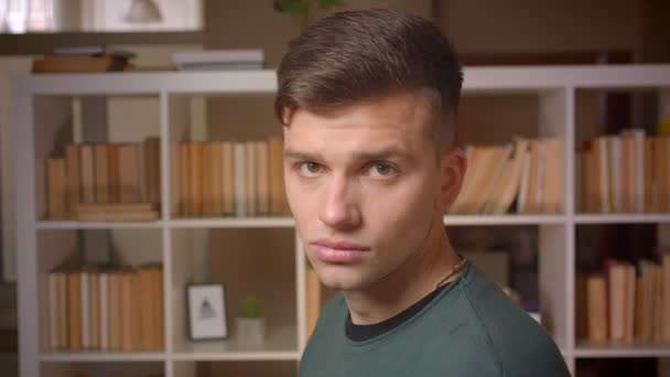 Portret van jonge mannelijke student draait naar camera en horloges ernstig in het staande in de bibliotheek. — Stockvideo