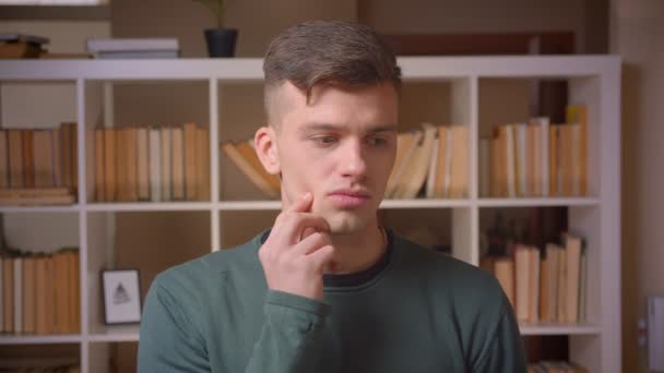 Retrato de un joven estudiante siendo reflexivo obtiene una visión y se alegra en la biblioteca . — Vídeo de stock