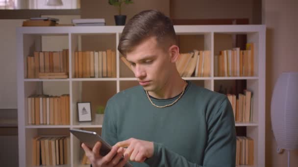 Ritratto di giovane studente maschio si accende l'applicazione su tablet mostra schermo cromato verde e gesti pollice-up in biblioteca . — Video Stock