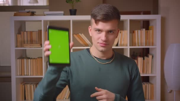 Portrét mladého mužského studenta zapne aplikaci na tabletu ukazuje zelenou Chroma obrazovku a palec v knihovně.