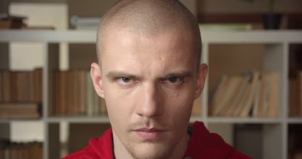 Retrato de close-up do jovem estudante masculino caucasiano atraente olhando para a câmera na biblioteca da faculdade dentro de casa com estantes no fundo — Vídeo de Stock