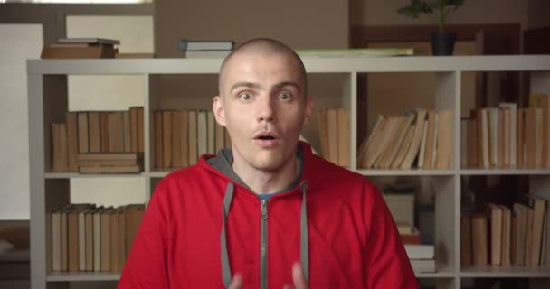 Closeup portrét mladého atraktivního bělošského studenta, vzrušeného a šokového pohledu na kameru v univerzitní knihovně uvnitř — Stock video