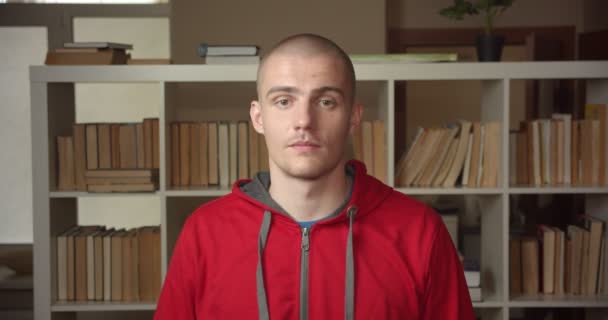 Крупный план портрета молодого привлекательного кавказского студента, который кивает головой, показывая согласие, глядя в камеру в библиотеке колледжа в помещении — стоковое видео