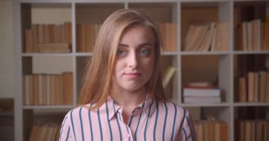 Kolej kitaplığında utangaçlık ile gülümseyen kamera bakarak genç güzel beyaz kadın öğrencinin kapatmak portre