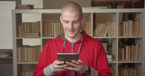 Close-up portret van jonge aantrekkelijke Kaukasische mannelijke student sms'en op de Tablet in het College bibliotheek binnenshuis — Stockvideo