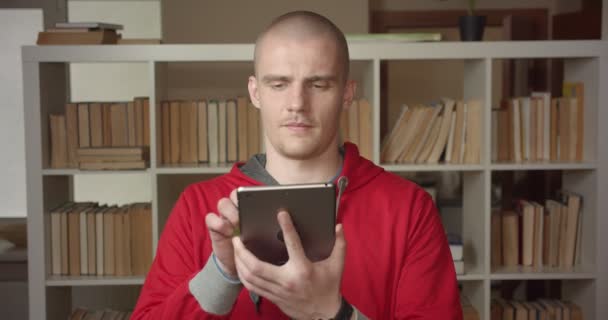 Retrato de close-up de jovem estudante masculino caucasiano atraente usando o tablet e mostrando tela de croma verde para câmera na biblioteca da faculdade dentro de casa — Vídeo de Stock