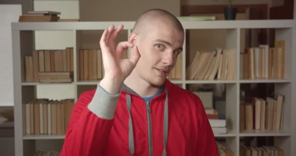 Närbild porträtt av unga attraktiva kaukasiska manliga studenten visar okej skylt tittar på kameran i College biblioteket inomhus — Stockvideo