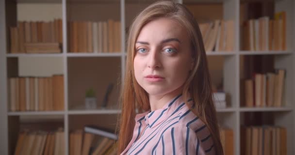 Closeup portrait of young pretty caucasian female student turning and looking at camera in the college library — Stock Video