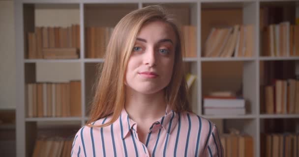 Close-up portret van jonge mooie Kaukasische vrouwelijke student glimlachen met vertrouwen te kijken naar de camera in het College bibliotheek — Stockvideo