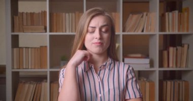 Genç güzel beyaz kadın öğrenci düşünceli olmak ve kolej Kütüphanesi kamera bakarak bir fikir alma portre