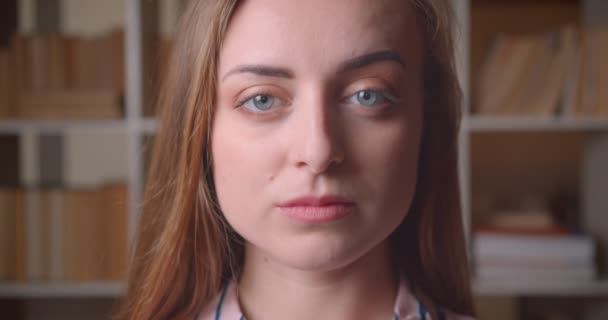Närbild porträtt av unga vackra kaukasiska kvinnlig elev tittar på kameran i College biblioteket inomhus — Stockvideo