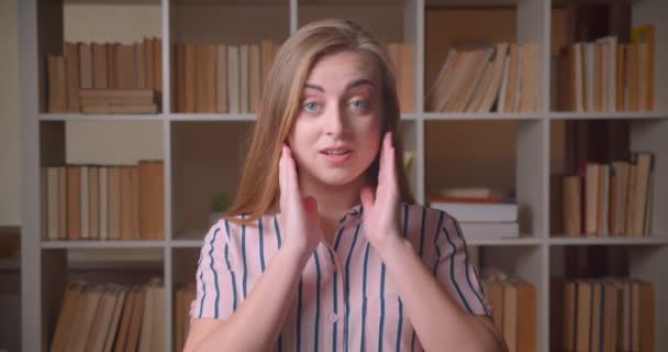 Primer plano retrato de joven bastante caucásica estudiante sonriendo con emoción mirando la cámara en la biblioteca de la universidad en el interior — Vídeo de stock