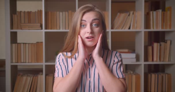 Closeup portré fiatal vidám kaukázusi női hallgató, hogy izgatott, és meglepett nézi kamera a főiskola könyvtár — Stock videók