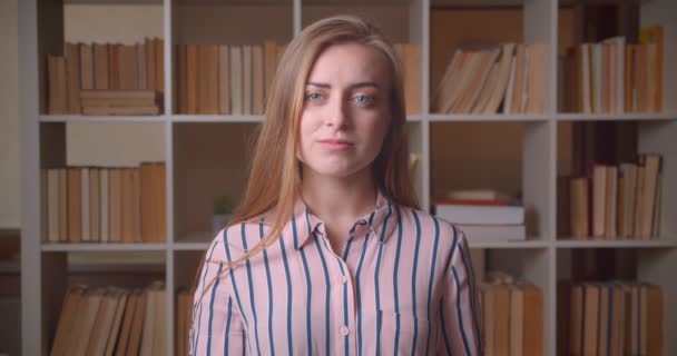 Zbliżenie portret młodego całkiem kaukaski studentka istota mylić patrząc na kamerę w bibliotece kolegium — Wideo stockowe