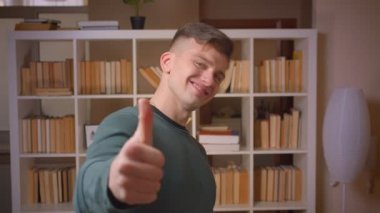 Genç erkek öğrenci jestleri portresi thumb-up anlaşma göstermek ve kütüphanede gibi.
