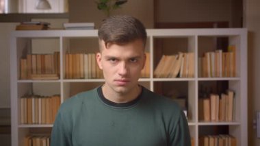 Kütüphanede duran kameraya ağır bir şekilde izleyen genç erkek öğrenciportresi.