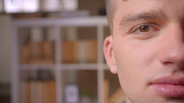 Портрет наполовину обличчя молодого студента-чоловіка посміхається чарівно в камеру, яка рада в бібліотеці . — стокове відео