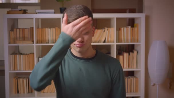 Portrét mladého mužského studenta gestikulky facepalm symbol pokrývající obličej s rukou v knihovně. — Stock video