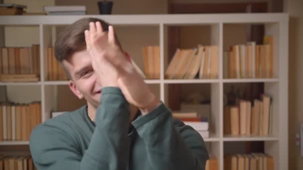 Portret van jonge mannelijke student voert vreemde en grappige dansen om de muziek wordt cool en ontspannen in de bibliotheek. — Stockvideo