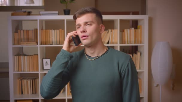 Retrato de un joven estudiante masculino que tiene una importante pantalla de voz en el teléfono inteligente que está atento en la biblioteca . — Vídeos de Stock