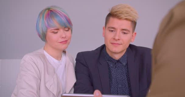 Zbliżenie strzelać młodej pięknej pary Hipster kupując mieszkanie rozmawiając z realtorem siedząc przy stole z tabletem w pomieszczeniu — Wideo stockowe