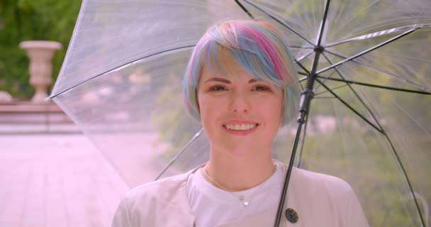 Closeup portrait of young cosplay caucasian female with dyed hair holding an umbrella looking at camera smiling happily outdoors in the park