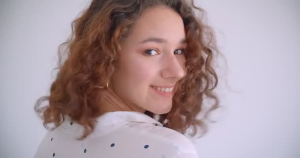 Zbliżenie strzelać młodego dość długowłosy kręcone kaukaski kobiece uśmiechnięty szczęśliwy toczenia i patrząc na aparat z tłem na białym tle — Wideo stockowe
