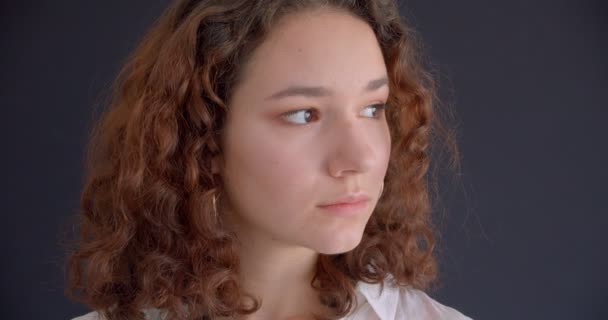 Nahaufnahme Porträt der jungen ziemlich langhaarigen lockigen kaukasischen Frau Blick auf die Kamera mit Hintergrund isoliert auf grau — Stockvideo