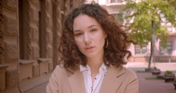 Closeup portrait of young long haired curly caucasian female student looking at camera standing outdoors on the street — Stock Video