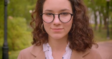 Genç uzun saçlı kıvırcık kafkas kız öğrencinin gözlüklerini sabitleme closeup portre bahçede açık havada duran kameraya bakarak neşeyle gülümseyerek