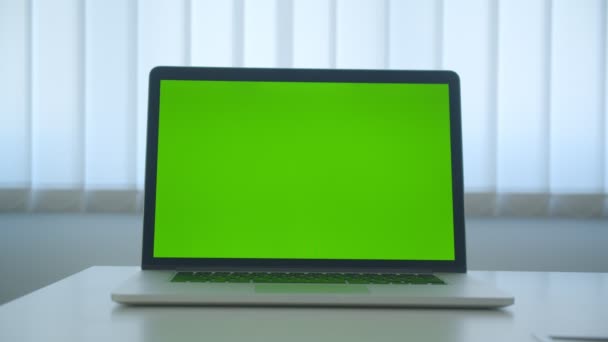 Disparo de primer plano de la computadora portátil con pantalla de clave de croma verde con aplicación puesta en la mesa en el interior de la oficina — Vídeo de stock