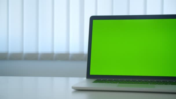 Disparo de primer plano de la computadora portátil con pantalla de clave de croma verde con anuncio en la mesa en el interior de la oficina — Vídeo de stock