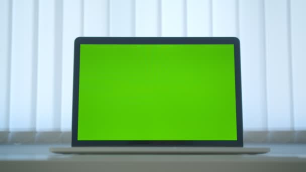 Disparo de movimiento de primer plano de la computadora portátil con pantalla de croma verde con anuncio en la mesa en el interior de la oficina — Vídeo de stock